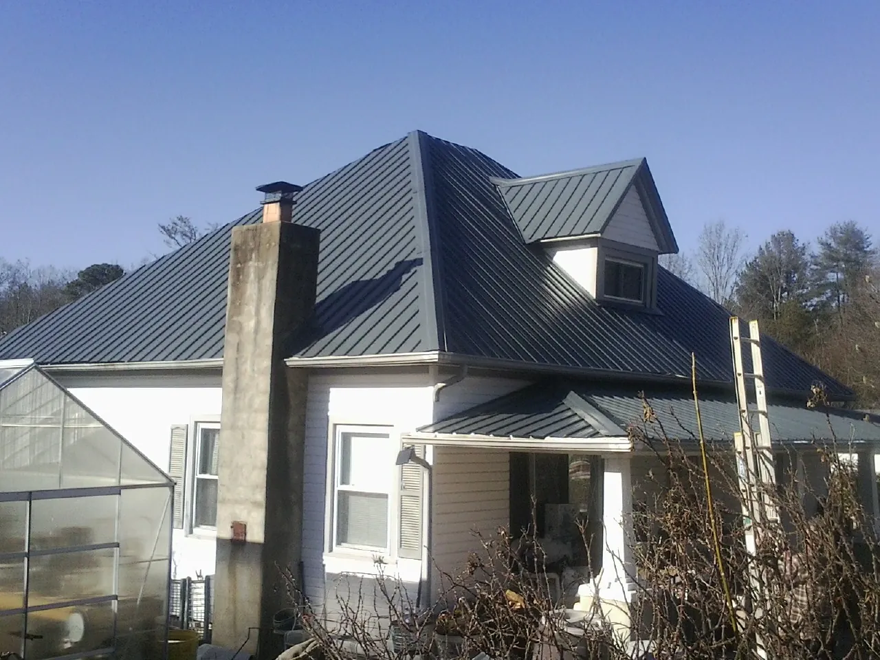 Dark blue standing seam metal roof on a white farmhouse with dormer — Slate & Tile Roof Repair by Roofing Brothers in Arbon