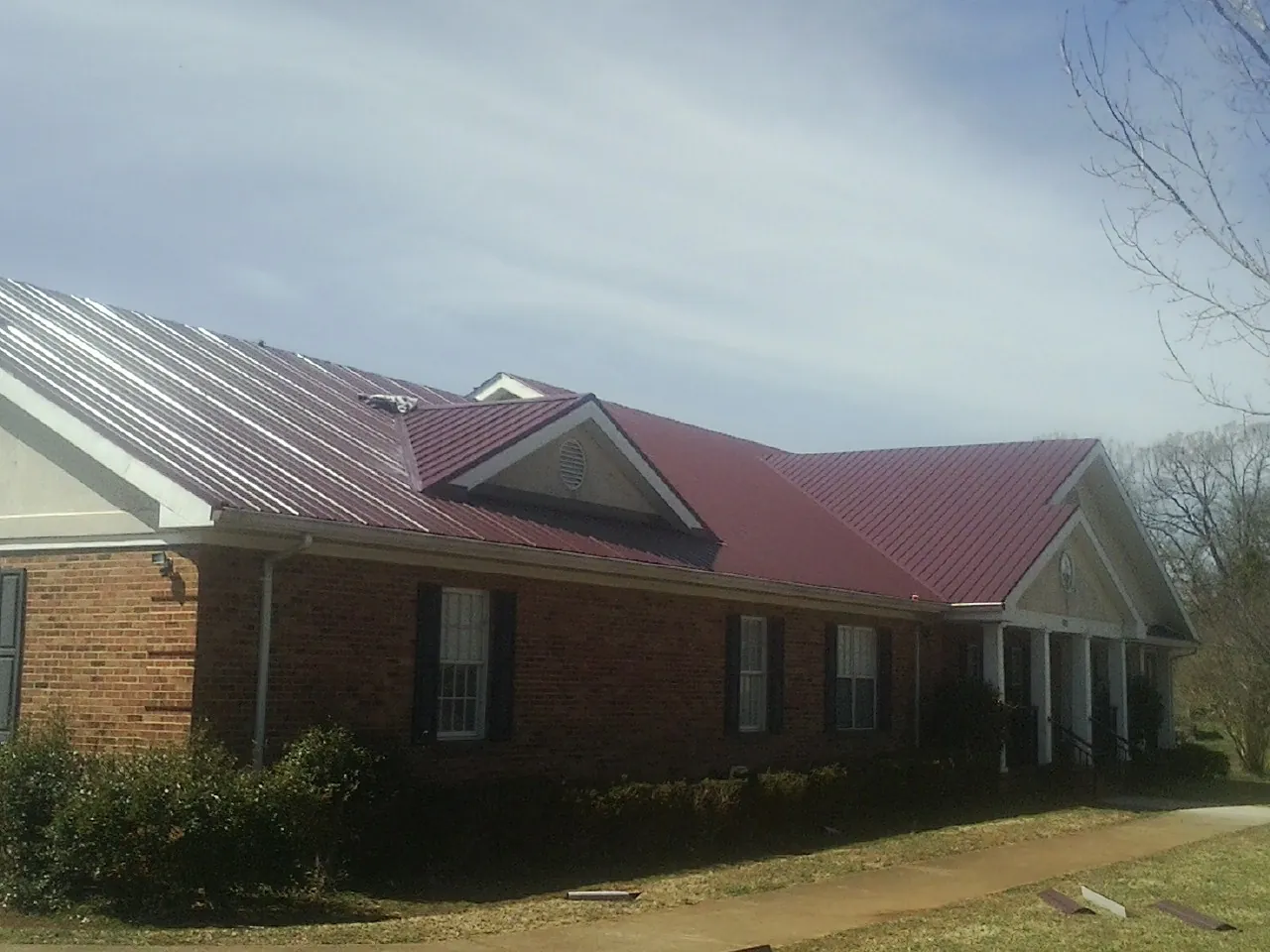 Red metal roof with gabled entries on a long brick building, from a Hail Damage Roof Repair job in Arbon