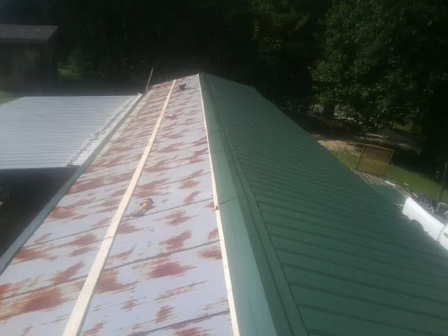 Old rusted panels beside newly installed green metal roofing — Wind Damage Roof Repair by Roofing Brothers in Arbon
