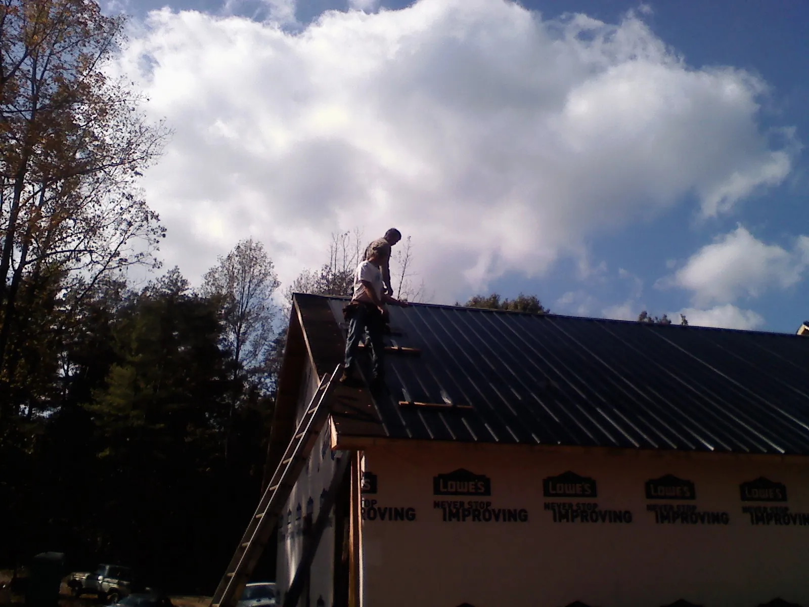 Roofer fastening dark metal panels high against a cloudy sky, from a Roof Inspection job in Arbon