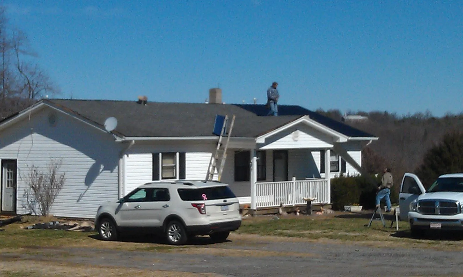 Roofers stripping shingles from a white ranch house roof in Arbon